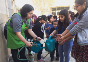 Ruby Zavala, Youth Gardens Coordinator for Texas A&M Agrilife Extension helps students at Schulze Elementary to fill water containers and wash soil from their hands. Photo by Christie Tavera