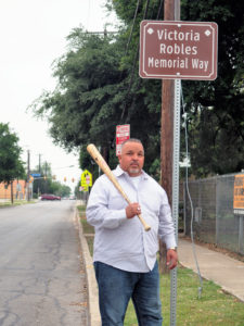 Pastor Jimmy Robles stands next to the recently named block, Victoria Robles Memory Way. The baseball bat is a symbol of challenges and lessons in his life. He actively assists his community by providing support and sharing his experiences. 